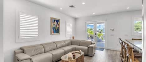 A modern living room with a sectional sofa, a glass coffee table, and a dining area with wooden chairs.