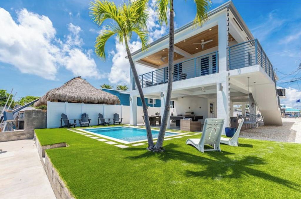 A two-story house with a pool, outdoor seating, and a thatched-roof structure.