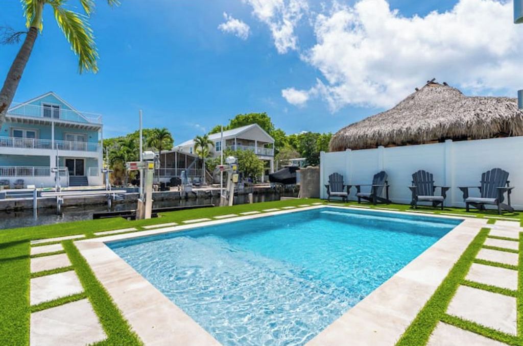 A swimming pool with a clear blue water, surrounded by a white wall and a thatched roof structure.