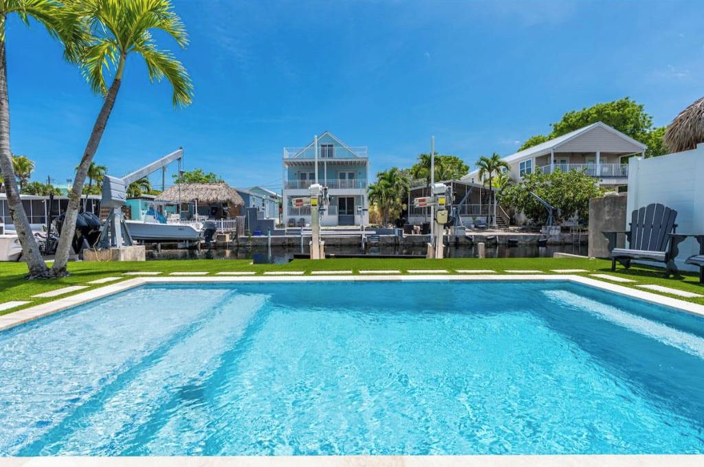 Une piscine à l’eau d’un bleu cristallin, entourée d’une pelouse bien entretenue et de palmiers.