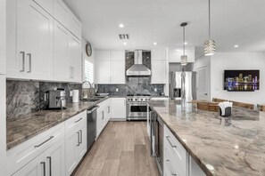 A modern kitchen with white cabinetry, a marble countertop, stainless steel appliances, and pendant lighting. - The Waves. (Key Largo)