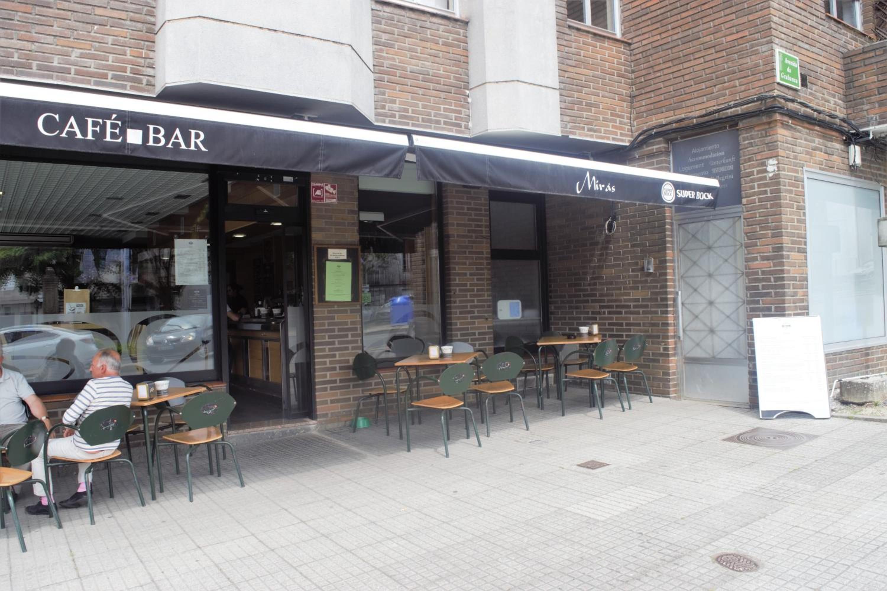 An outdoor café with tables and chairs, a covered entrance, and a sign for 'NIRAS SUPER BOKK'.
