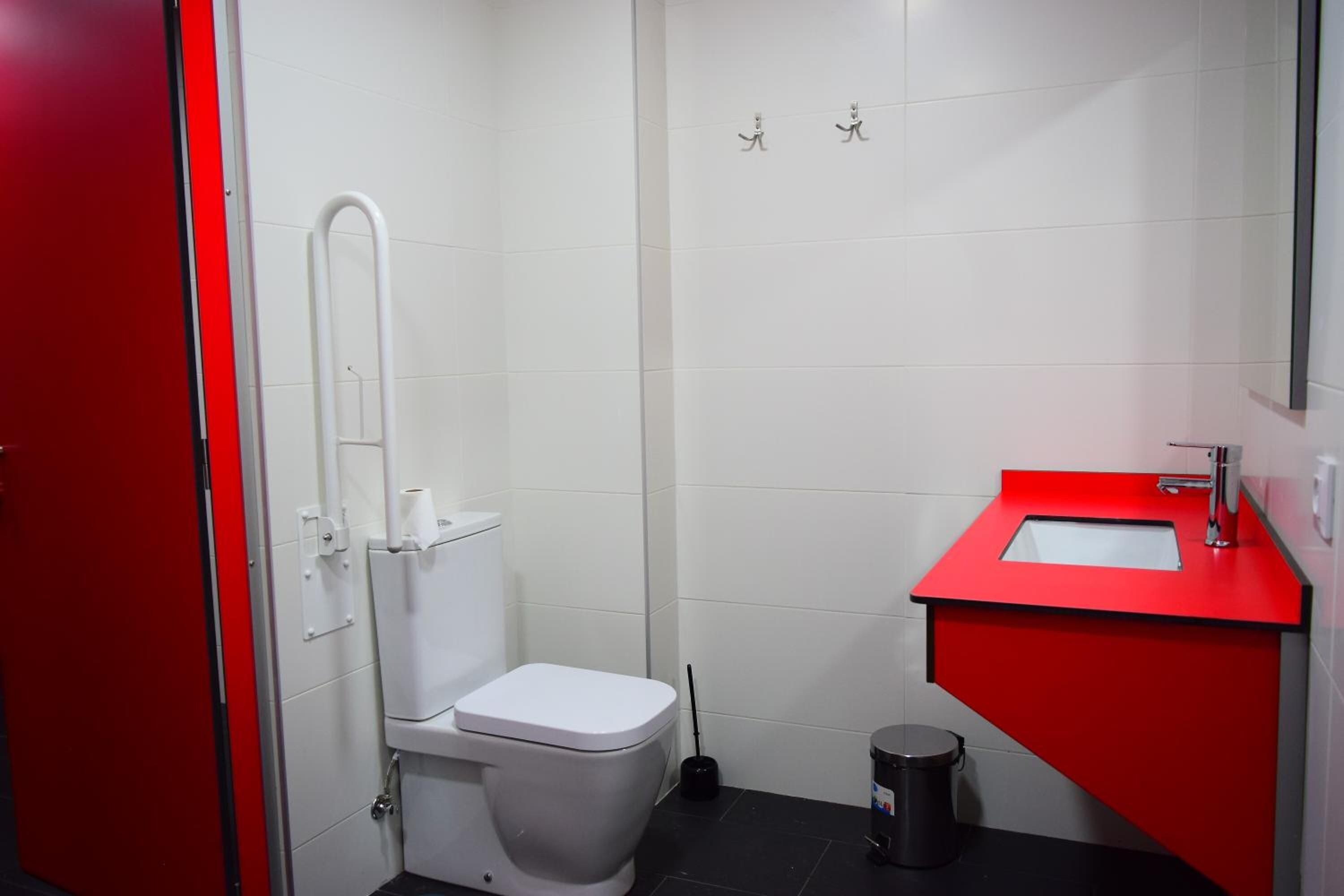 A compact bathroom with a white toilet, a red sink, and a black trash bin.