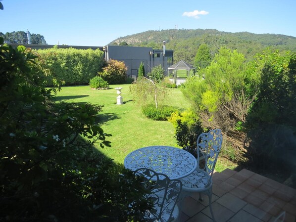 A garden with a patio table and chairs, a white birdbath, and a gazebo. - Golfview Lodge (Bowral)
