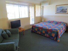 Una habitación con cama, televisión, sofá y ventana con persianas.