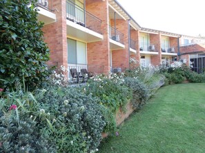 A multi-story hotel with balconies, a well-maintained garden, and a clear sky. - Golfview Lodge (Bowral)
