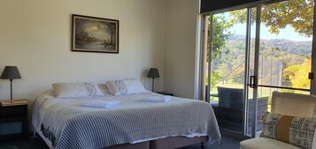 Habitación de hotel con cama, dos lámparas de noche, un cuadro en la pared y balcón con vistas al campo.