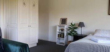 Un dormitorio con cama, mesita de noche, lámpara, planta, armario y estante con adornos.