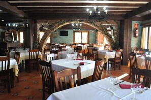 Un restaurante con varias mesas, sillas de madera y un arco de ladrillo.