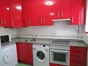 Una cocina compacta con armarios rojos, un microondas, una lavadora y un horno.