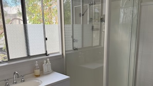 Ett badrum med en dusch som är avskärmad med glasväggar, ett vitt handfat med en spegel och ett fönster med frostat glas.