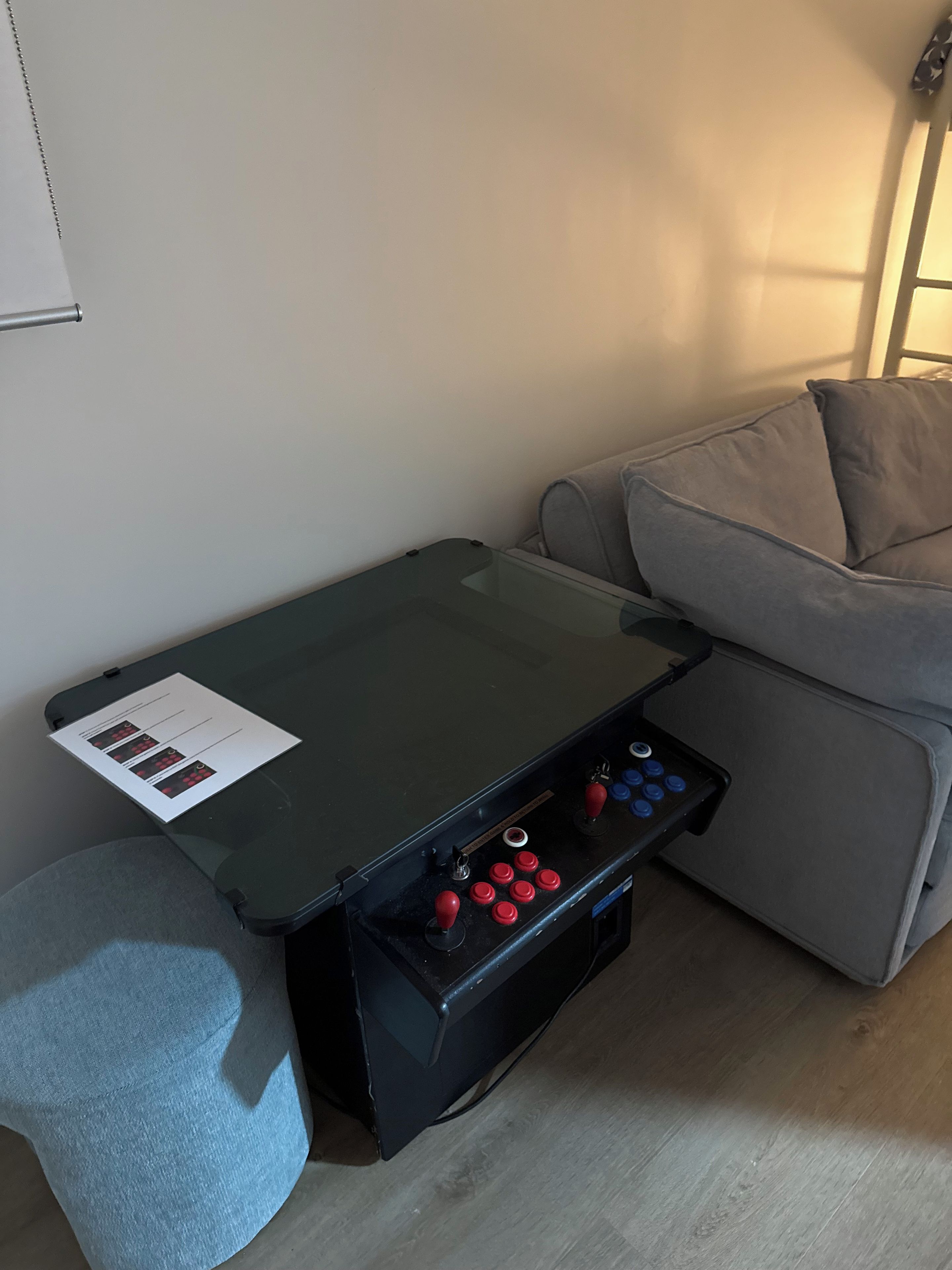 Een kamer met een speeltafel, een grijze bank en een klein krukje.