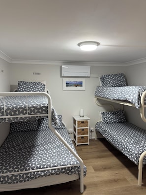 Une chambre avec des lits superposés, un climatiseur blanc, un tableau encadré au mur et une table de chevet avec une lampe.