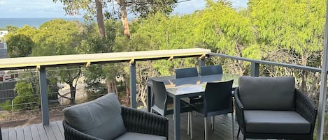 A covered outdoor deck with seating and a table, overlooking a natural landscape.