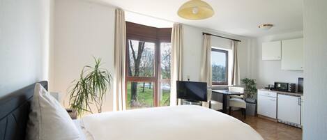 A modern bedroom with a large bed, a desk, and a kitchenette.