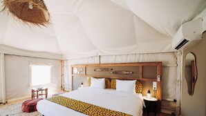 Une pièce aménagée comme une tente, avec un grand lit, une tête de lit en bois, des lampes de chevet et un luminaire suspendu.