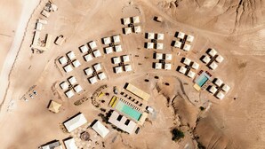 Vista aèria d'un complex turístic al desert, amb diverses tèntes, una piscina i alguns vehicles.