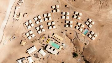 An aerial view of a desert resort with multiple tents, a swimming pool, and a few vehicles.