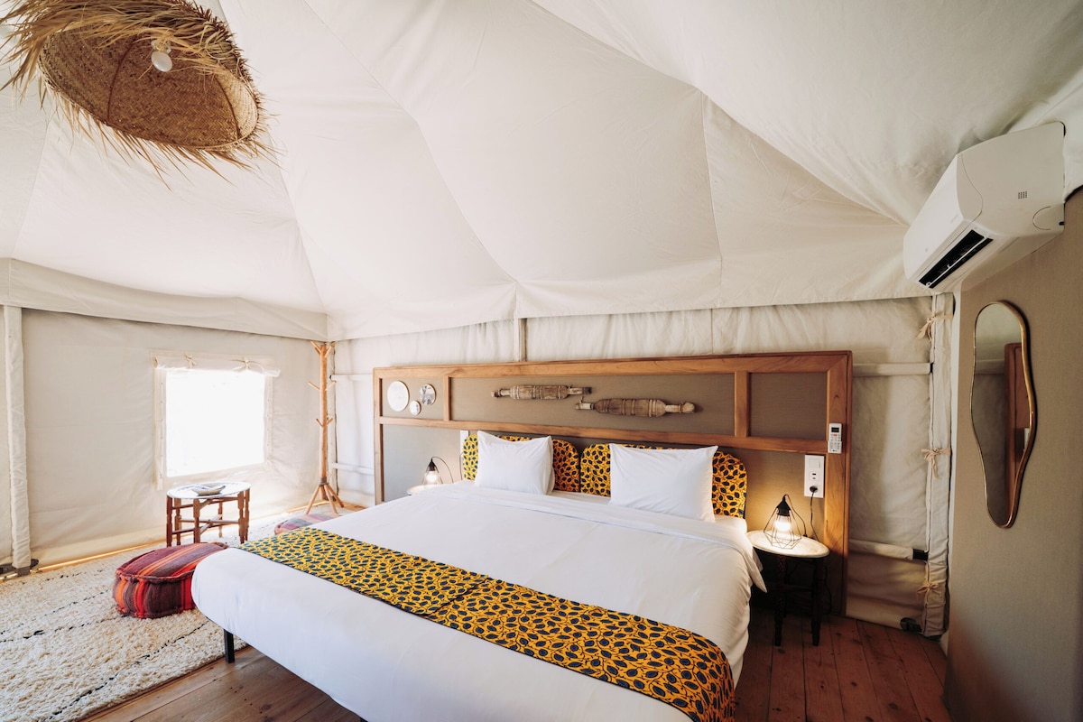 A tented room with a large bed, wooden headboard, bedside lamps, and a hanging light fixture.