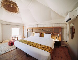 Una habitación con tienda de campaña, una cama grande, cabecera de madera, lámparas de noche y un candelabro colgante.