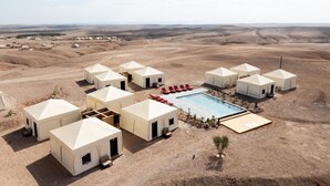Un complexe hôtelier situé dans le désert, comprenant plusieurs yourtes, une piscine et offrant une vue sur le paysage aride environnant.