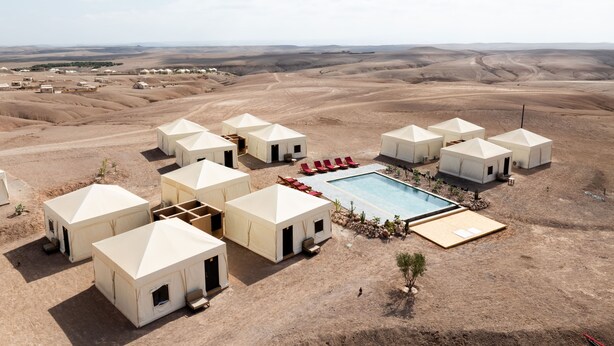 Un complex turístic al desert amb diverses iurts, una piscina i vista del paisatge àrid circumdant.