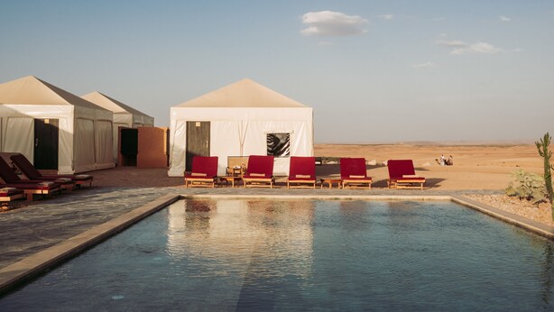 Un complexe hôtelier situé dans le désert, doté d’une piscine, de chaises longues rouges et de tentes.