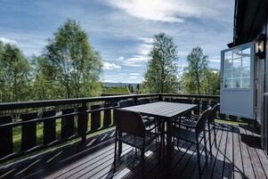 A wooden deck with a table and chairs, overlooking a landscape with trees and a distant view.
