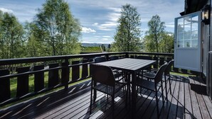 A wooden deck with a table and chairs, overlooking a landscape with trees and a distant view. - Bitigrenda N (Øystre Slidre)