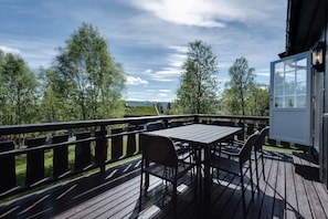 Una terraza de madera con una mesa y sillas, con vista a un paisaje con árboles y una vista distante.