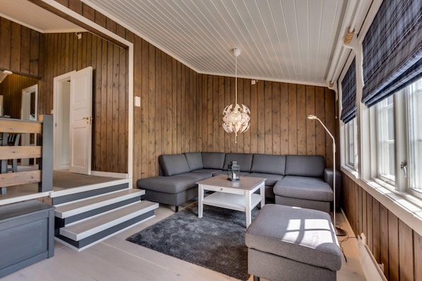 Una sala de estar moderna con un sofá seccional gris, una mesa de centro blanca y una escalera que sube a un nivel superior.