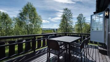 A wooden deck with a table and chairs, overlooking a landscape with trees and a distant view.
