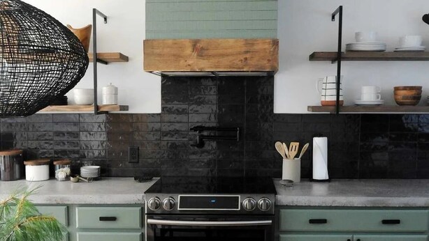 Cozinha moderna com fogão central, armários verdes e uma mesa de jantar posta com pratos e copos brancos.