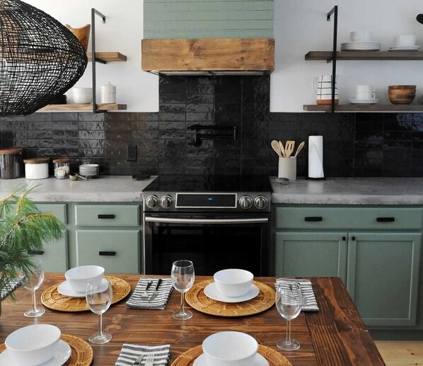 Een moderne keuken met een centraal geplaatst fornuis, groene kastjes en een eettafel gedekt met witte borden en glazen.