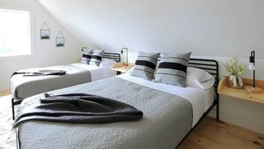 Quarto com duas camas, uma mesinha de cabeceira, luminária e janela.