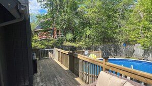 Um deck de madeira com piscina, um sofá de vime e um cercado de madeira.