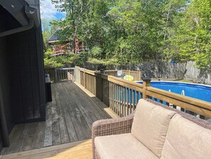 Een houten terras met een zwembad, een rieten bank en een houten omheining.