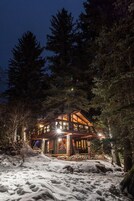 A cabin with a wooden exterior, surrounded by snow and trees, at night.