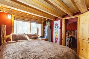 Acogedora habitación de cabaña de madera con una cama grande, una ventana con persianas y una puerta que da a un área de almacenamiento.