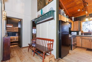 A wooden interior with a bench, a black refrigerator, and wooden cabinets.