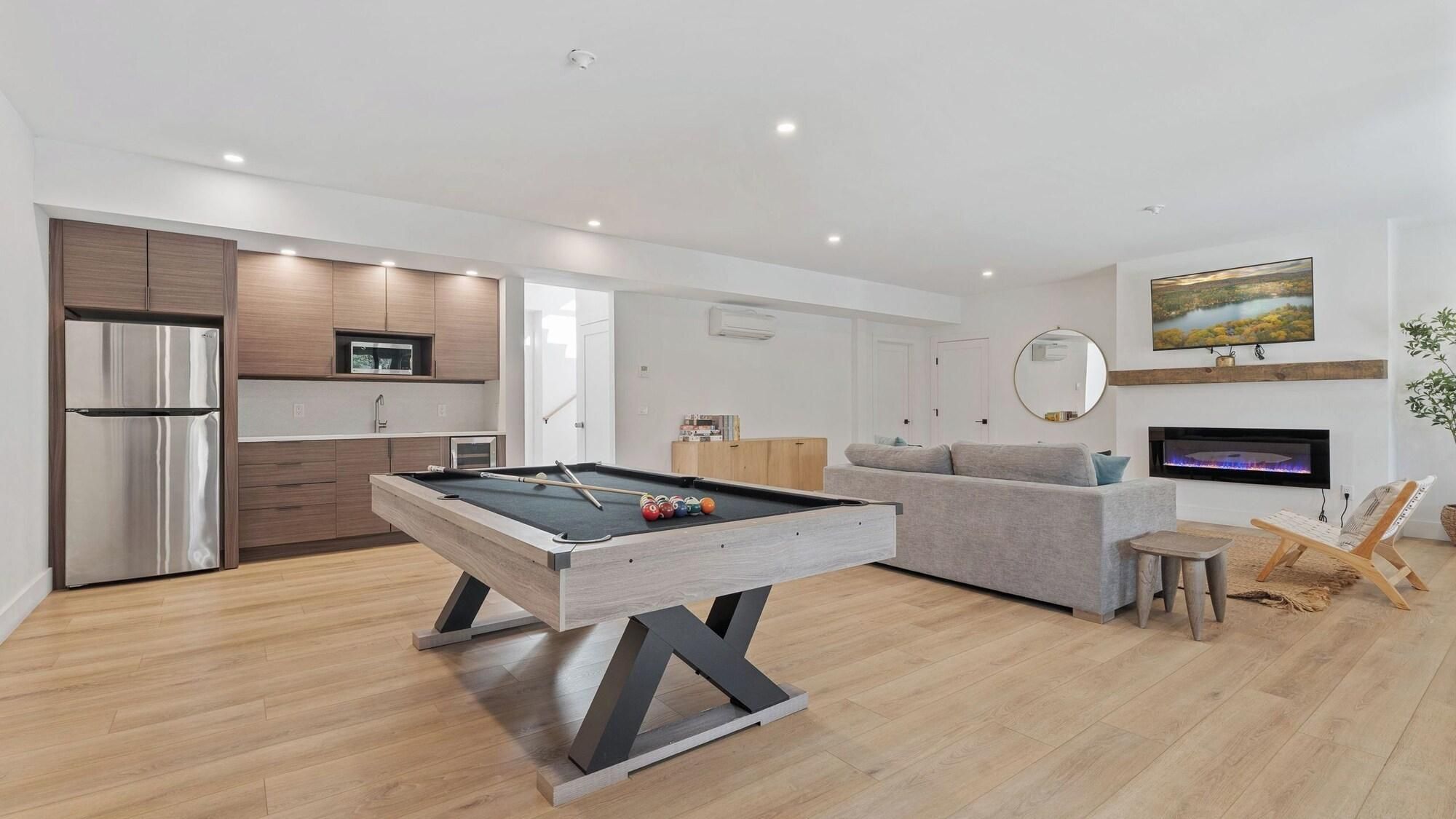 A modern living room with a pool table, a sofa, a TV, and a fireplace.