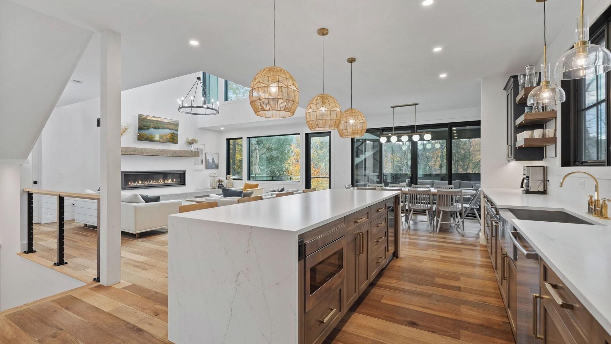 A modern kitchen with a large island, wooden cabinets, and pendant lighting.