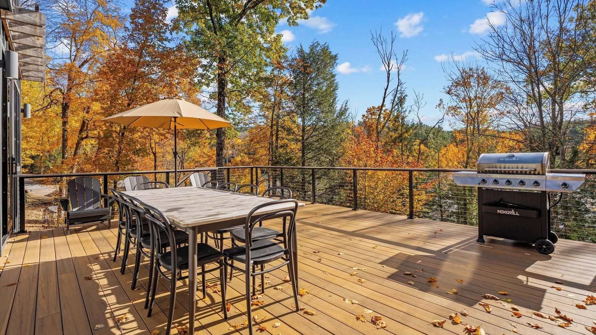 Eine Terrasse mit Grill, Tisch und Stühlen, umgeben von Herbstbäumen.