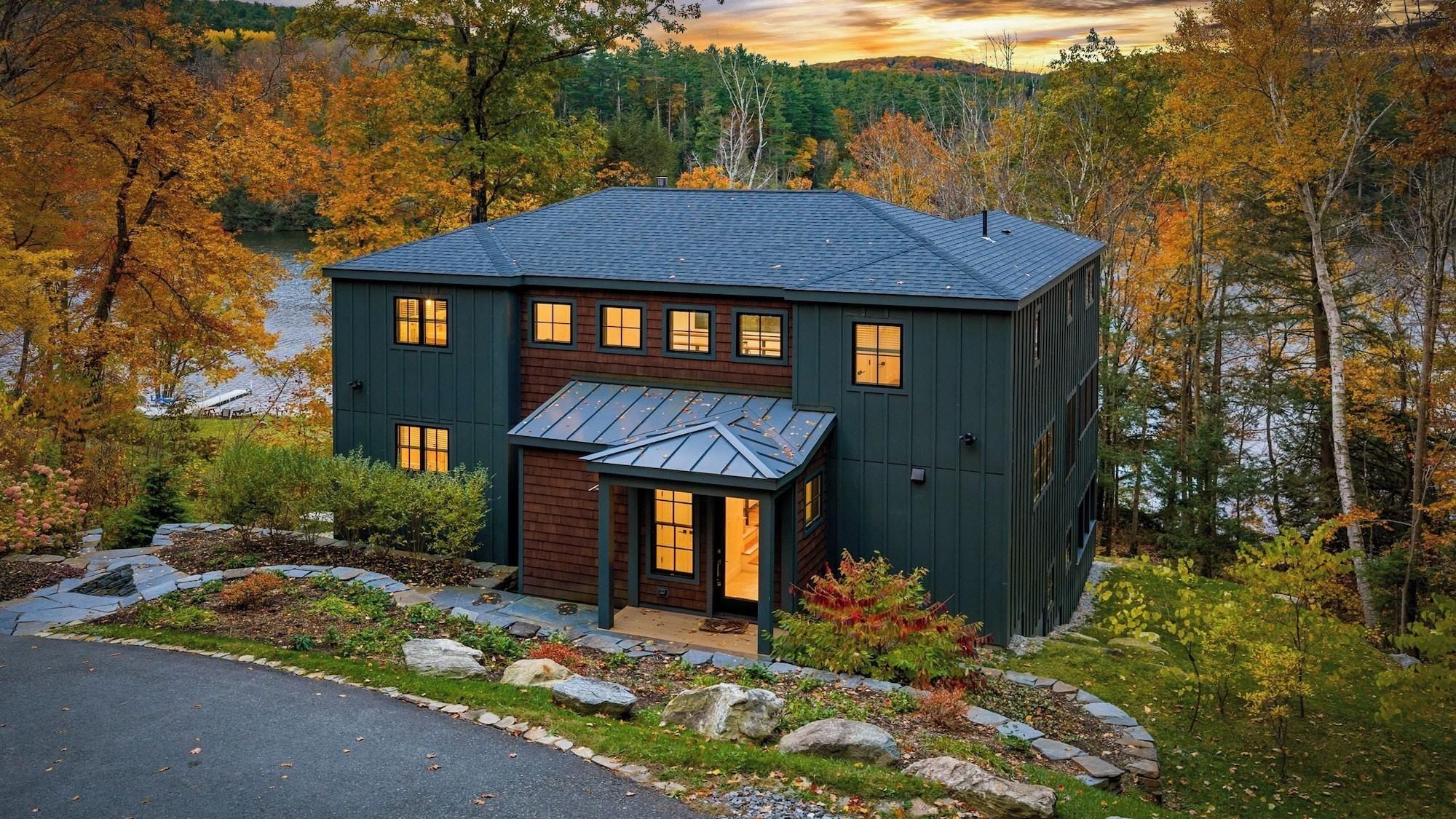 A two-story house with a dark exterior, a covered porch, and a view of a forested area.