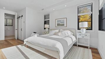 A modern bedroom with a bed, bedside tables, a window with blinds, and a door.