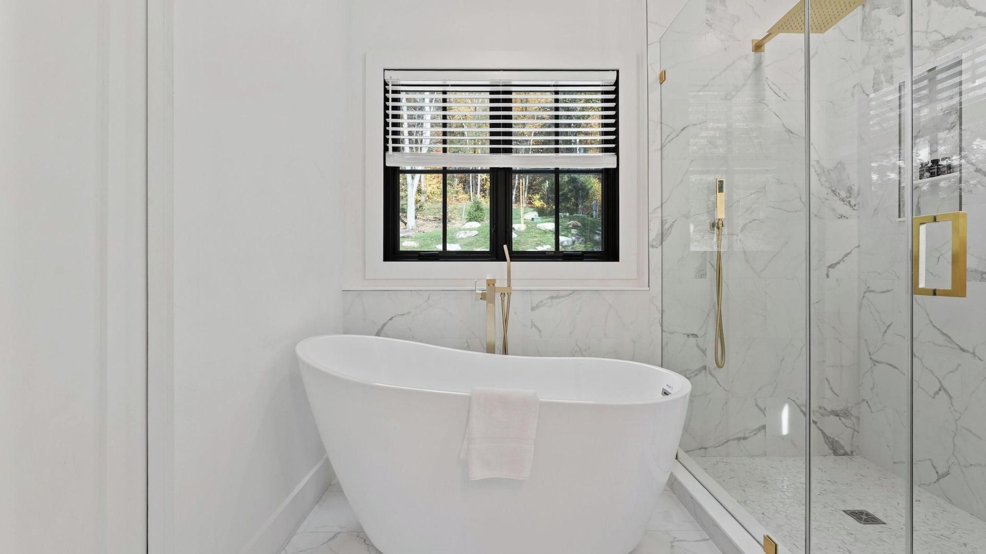 A modern bathroom with a freestanding bathtub, a shower enclosure, and a window with blinds.