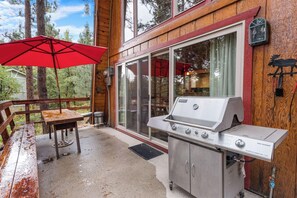 An outdoor patio with a grill, a red umbrella, and a view of the surrounding forest. - Zen Den (Big Bear Lake)