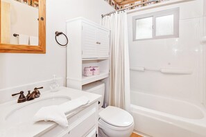 A bathroom with a white sink, a toilet, a shower with a curtain, and a mirror with a wooden frame. - Zen Den (Big Bear Lake)