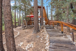 A wooden cabin with a staircase leading to a deck, surrounded by trees. - Zen Den (Big Bear Lake)