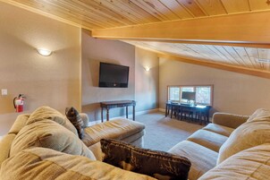 Una sala de estar acogedora con techo alto, un televisor de pantalla plana en la pared, una zona de comedor con ventana y un extintor en la pared.